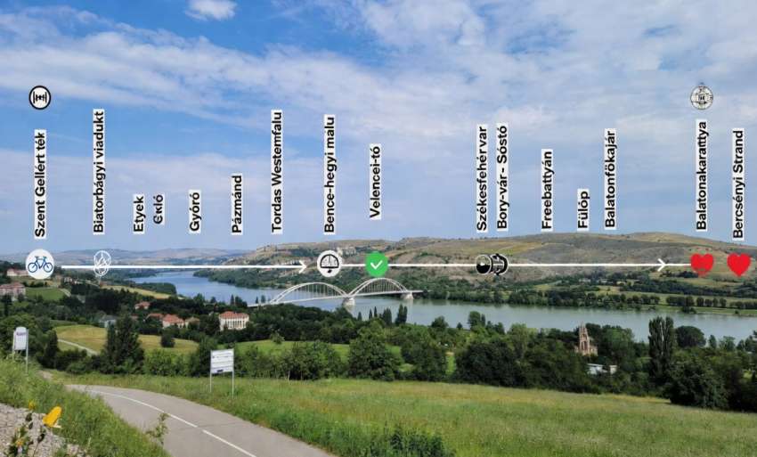 Budapest-Balaton kerékpárút látképe: kerékpáros út a Velencei-tó partján, háttérben a Bence-hegyi kilátó és a tó tükre, előtérben gondozott kerékpárút zöld fűvel szegélyezve