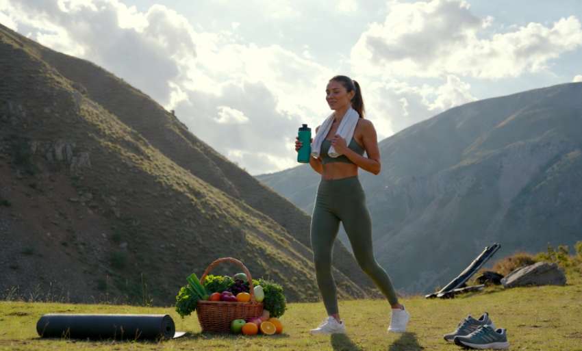 Nő edz outdoor hegyi tájban, egészséges gyümölcsökkel és sportfelszereléssel – fogyás és fitnesz 2026